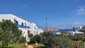 Edificio costero con paredes blancas y detalles azules, rodeado de vegetación y con vistas al mar.