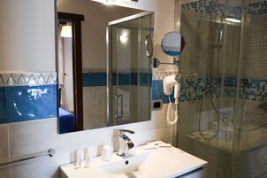 Un bagno con un lavandino bianco, uno specchio, un soffione a mano e una cabina doccia in vetro.