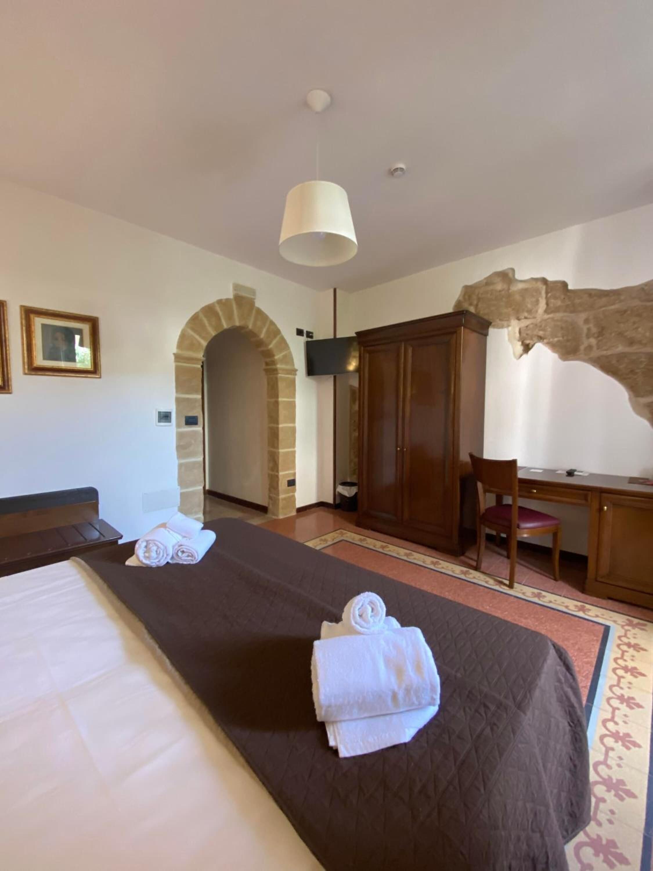Une chambre d’hôtel avec deux lits, un bureau, une chaise, une télévision et une porte en pierre en forme d’arc.