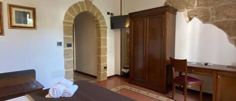 A hotel room with two beds, a desk, a chair, a TV, and an arched stone doorway.