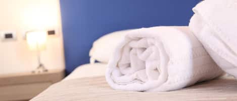 A neatly folded white towel on a bed with a wooden headboard and a bedside table with a lamp.