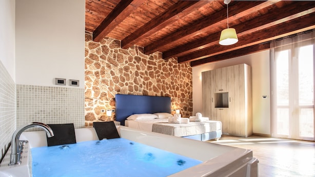 A modern bathroom with a stone wall, a large bathtub, and a wooden ceiling. - Double B - Maison De Charme (Alghero)
