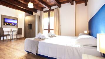 Habitación de hotel con techo de madera, cama con ropa blanca, escritorio con sillas y televisor en la pared.