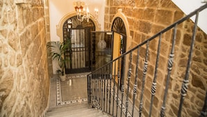 A stone-walled staircase with a wrought iron railing, leading to a door with a 'B' sign, and a chandelier above. - Double B - Maison De Charme (Alghero)