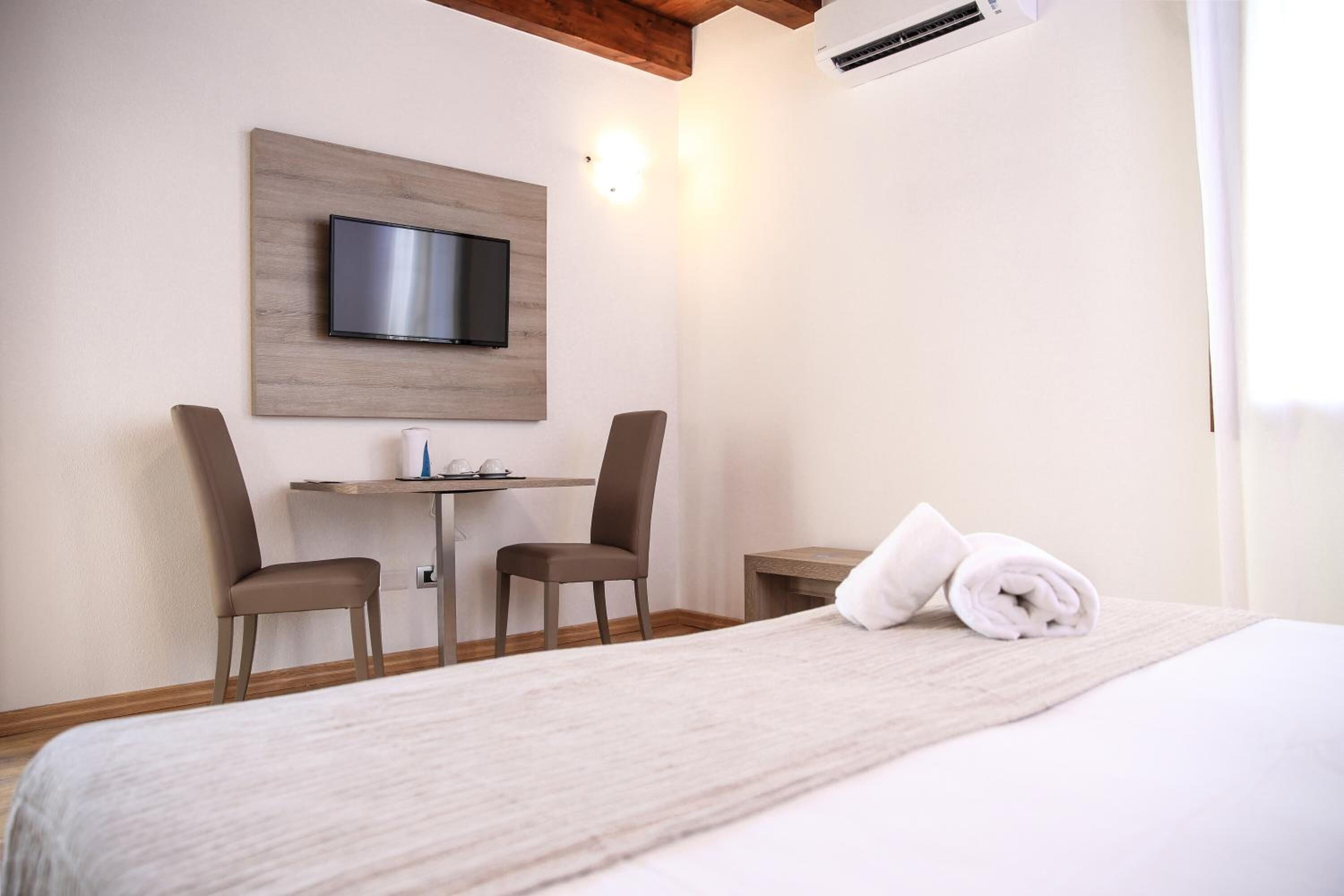 Une chambre d’hôtel comprenant un lit, un bureau, deux chaises, un téléviseur à écran plat fixé sur un panneau en bois et une serviette roulée posée sur le lit.