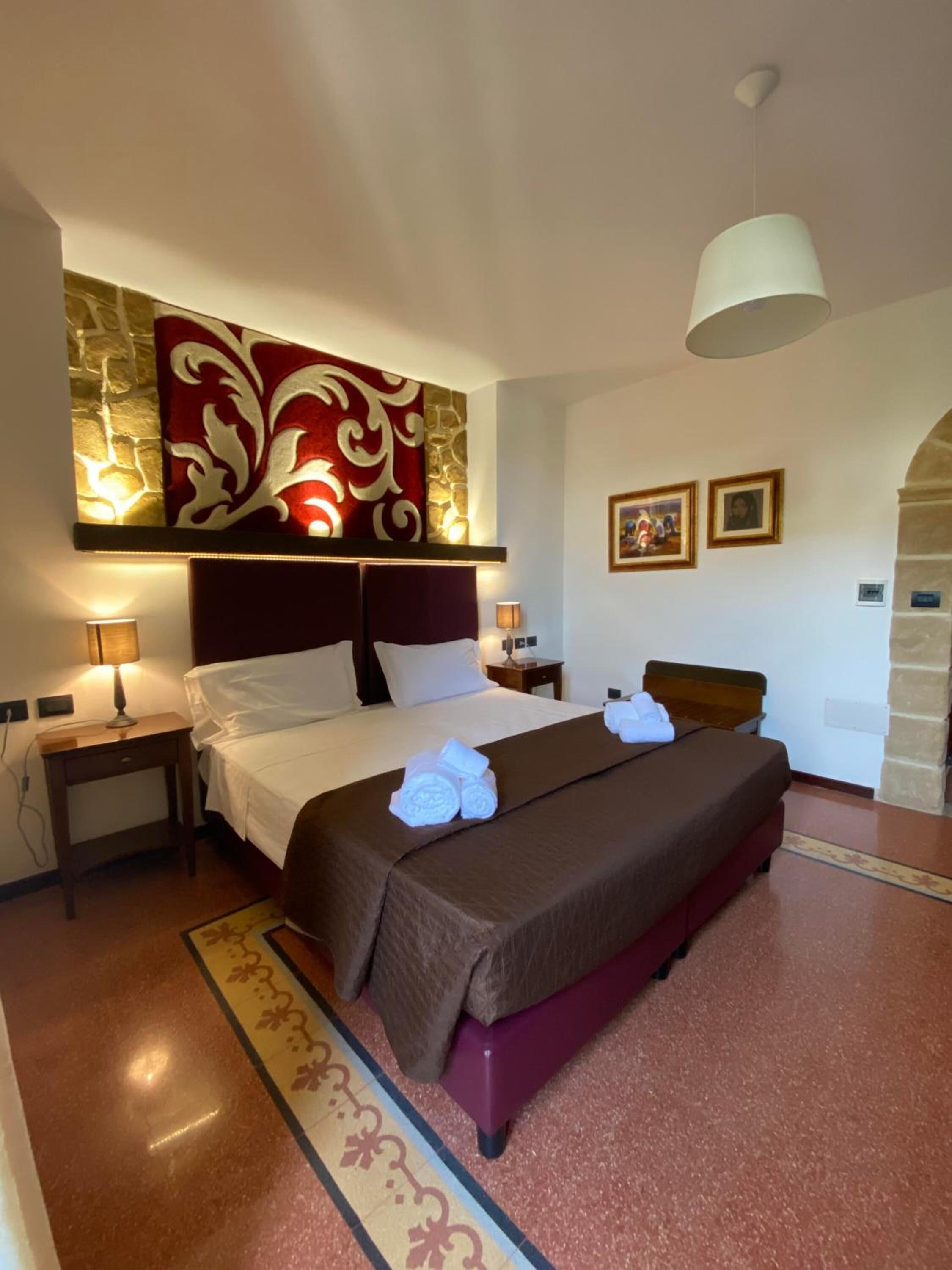 Une chambre d’hôtel avec un grand lit, deux tables de chevet avec des lampes, un élément décoratif mural et un petit cadre photo accroché au mur.