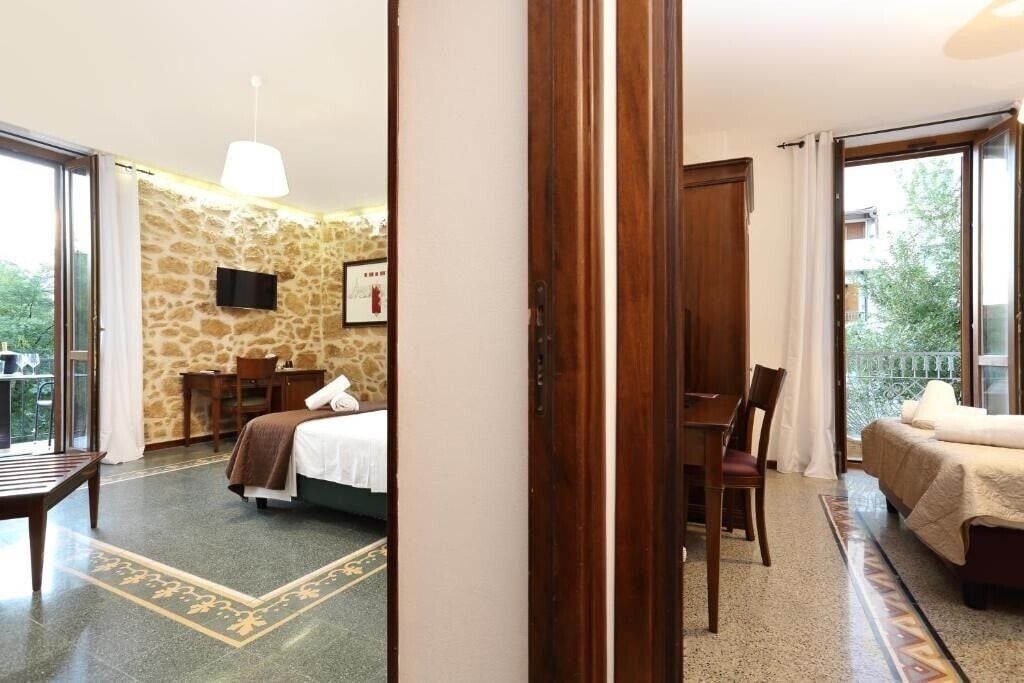 A hotel room with a stone wall, a bed, a desk, and a chair.