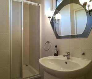 A bathroom with a white sink, a mirror with lights, and a shower.