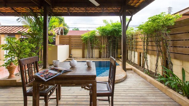 A covered outdoor area with a wooden table and chairs, a small pool, and surrounding greenery. - Hua Hin Home (Hua Hin)