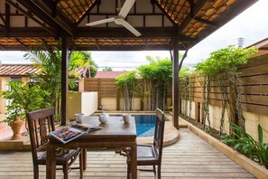 A covered outdoor area with a wooden table and chairs, a small pool, and surrounding greenery. - Hua Hin Home (Hua Hin)