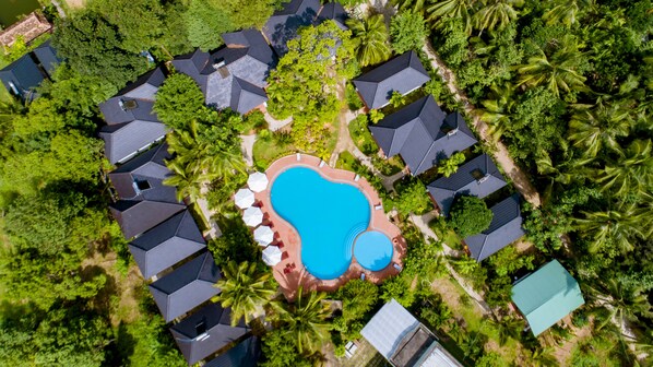 An aerial view of a resort with multiple bungalow-style buildings, a central swimming pool, and lush tropical vegetation. - Long Mountain Be Home 5 Resort (Phu Quoc)