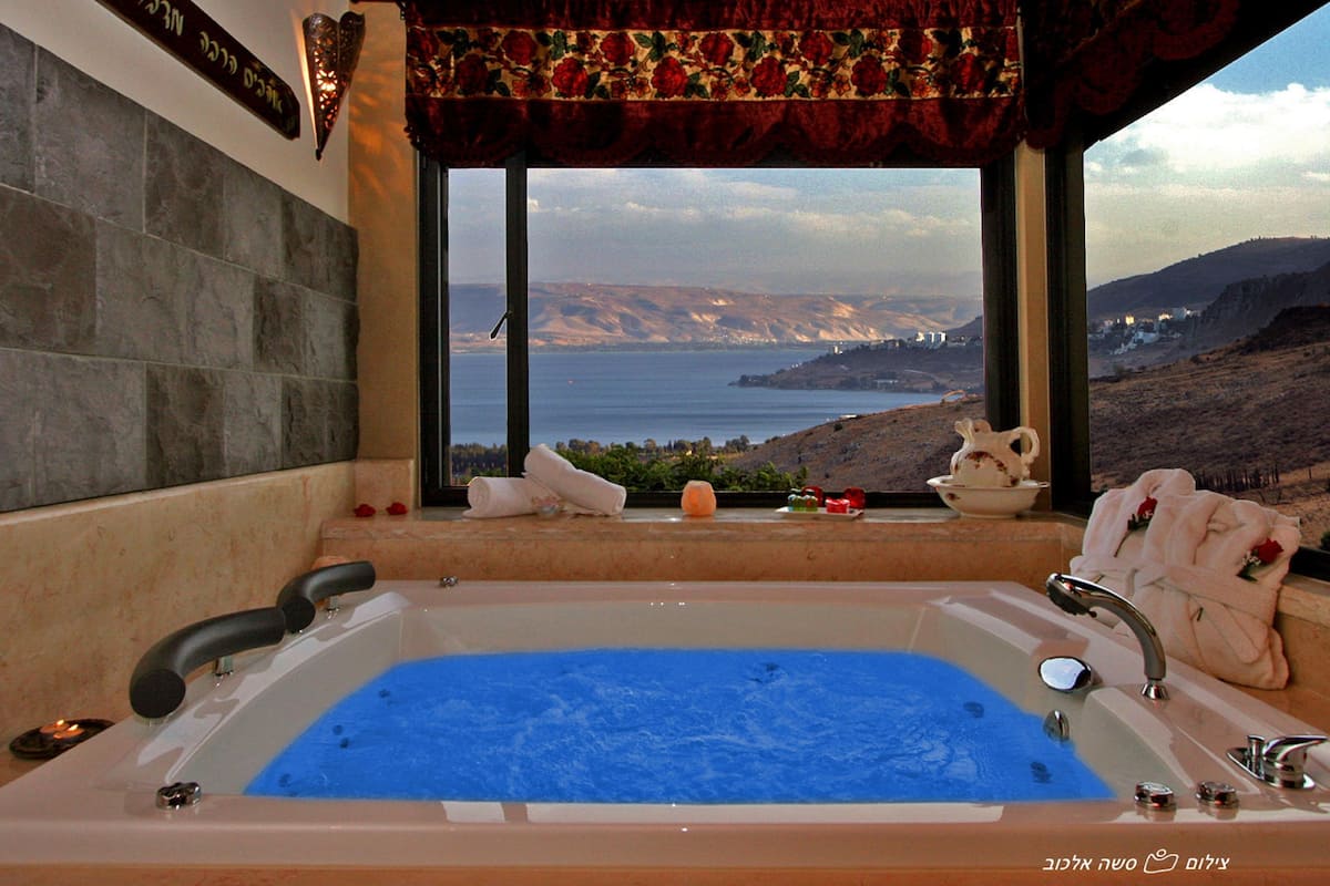 A bathroom with a large bathtub, a view of the sea, and a decorative curtain.