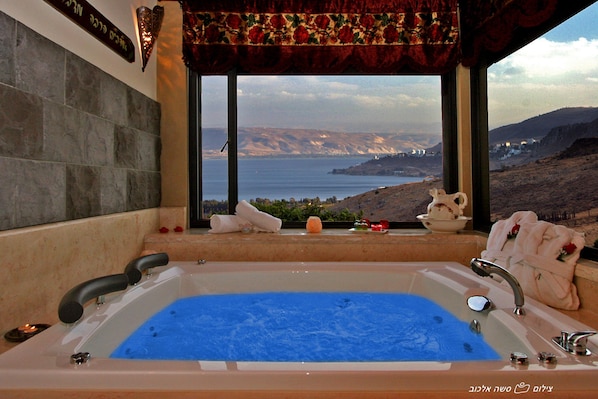 A bathroom with a large bathtub, a view of the sea, and a decorative curtain. - Ayelet Ahavim Hotel (Merom HaGalil)