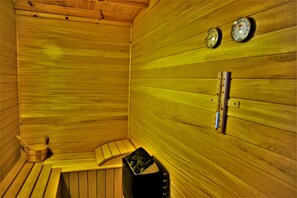 A sauna with wooden walls, a bench, a bucket, and two wall-mounted clocks. - Ayelet Ahavim Hotel (Merom HaGalil)