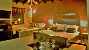 A hotel room with a large bed, a sitting area with a table, a TV, and a bathtub. - Ayelet Ahavim Hotel (Merom HaGalil)