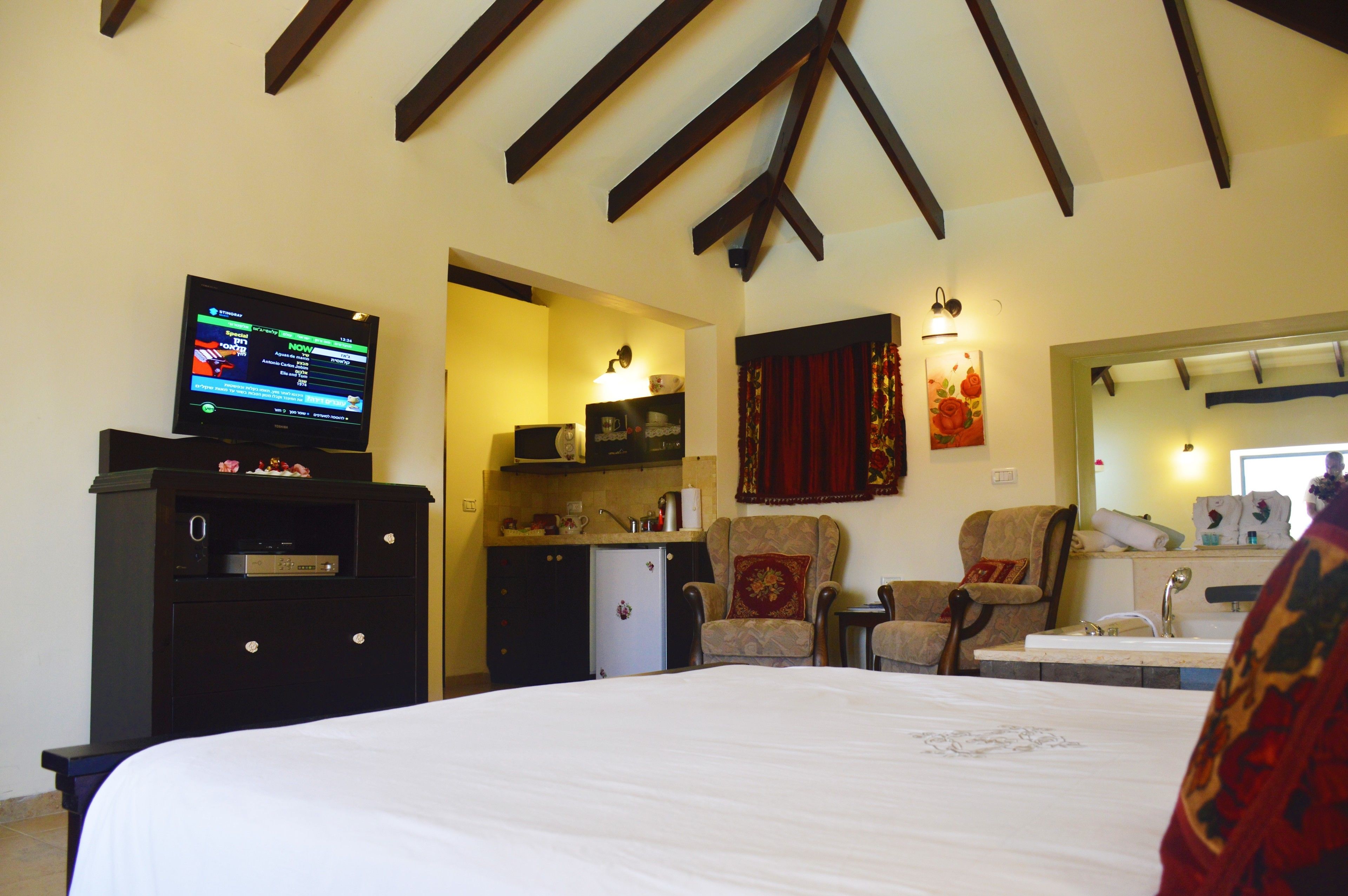Quarto de hotel com uma cama, televisão, escrivaninha com computador, cadeira, pequeno espaço de cozinha e banheiro.