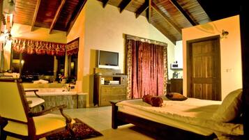 A bedroom with a bed, a chair, a TV, a dresser, and a window with curtains.
