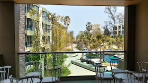 A balcony with white chairs and a view of a swimming pool, surrounded by greenery and modern buildings. - Lumpini Park Beach Cha-Am Seaview A01-207 (Cha-am)