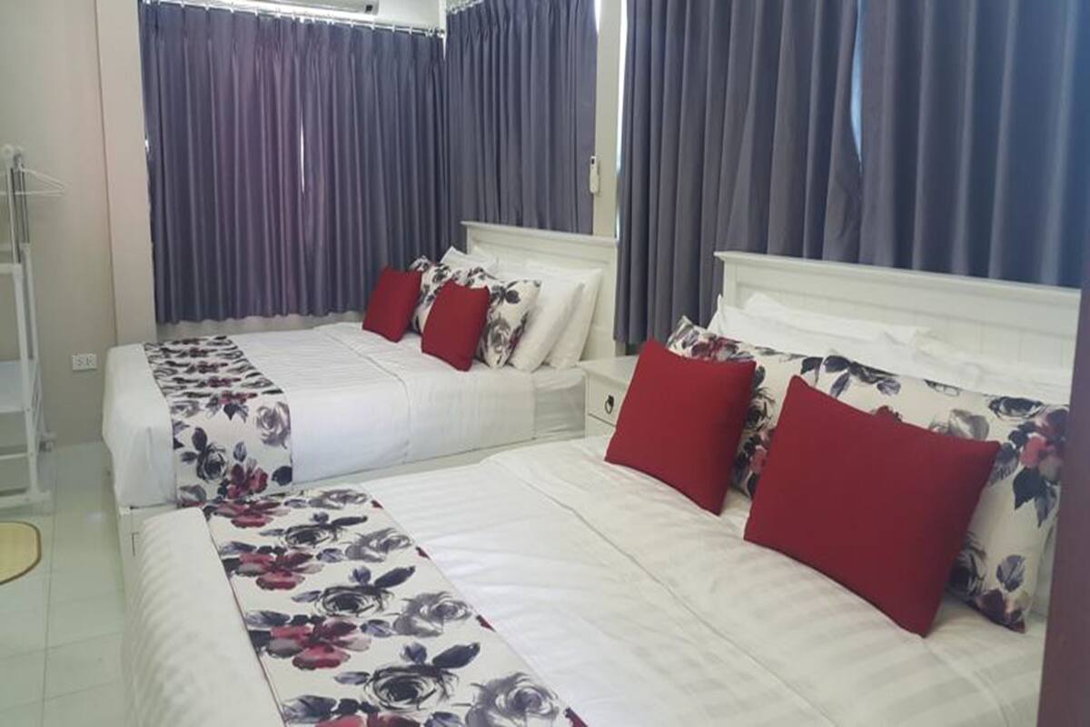 A hotel room with two beds, each with floral bedding and red pillows, a bedside table, and a wardrobe.