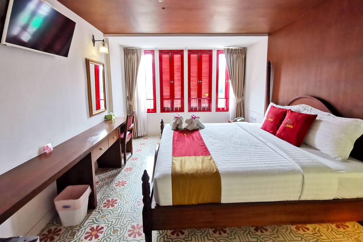 Une chambre d’hôtel avec un lit, un bureau, une chaise, une télévision et une fenêtre avec des volets rouges.