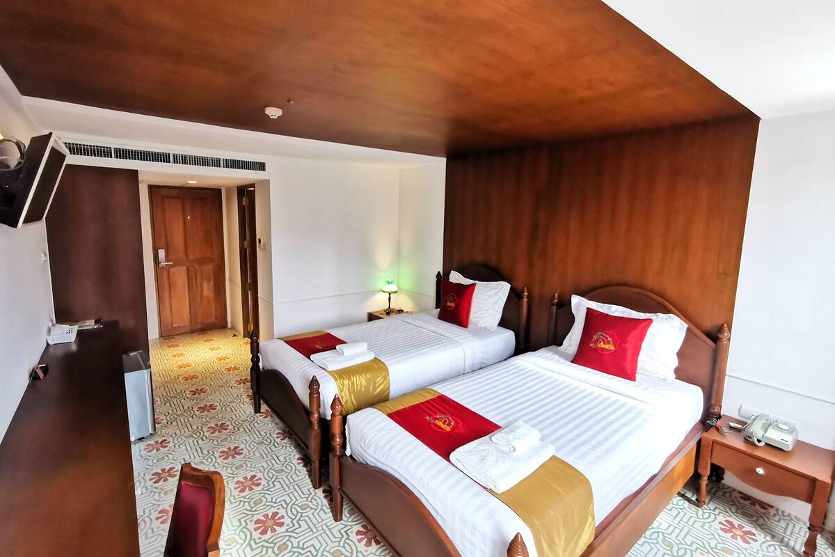 Une chambre d’hôtel avec deux lits, des têtes de lit en bois, un sol à motifs, un bureau et un téléviseur fixé au mur.