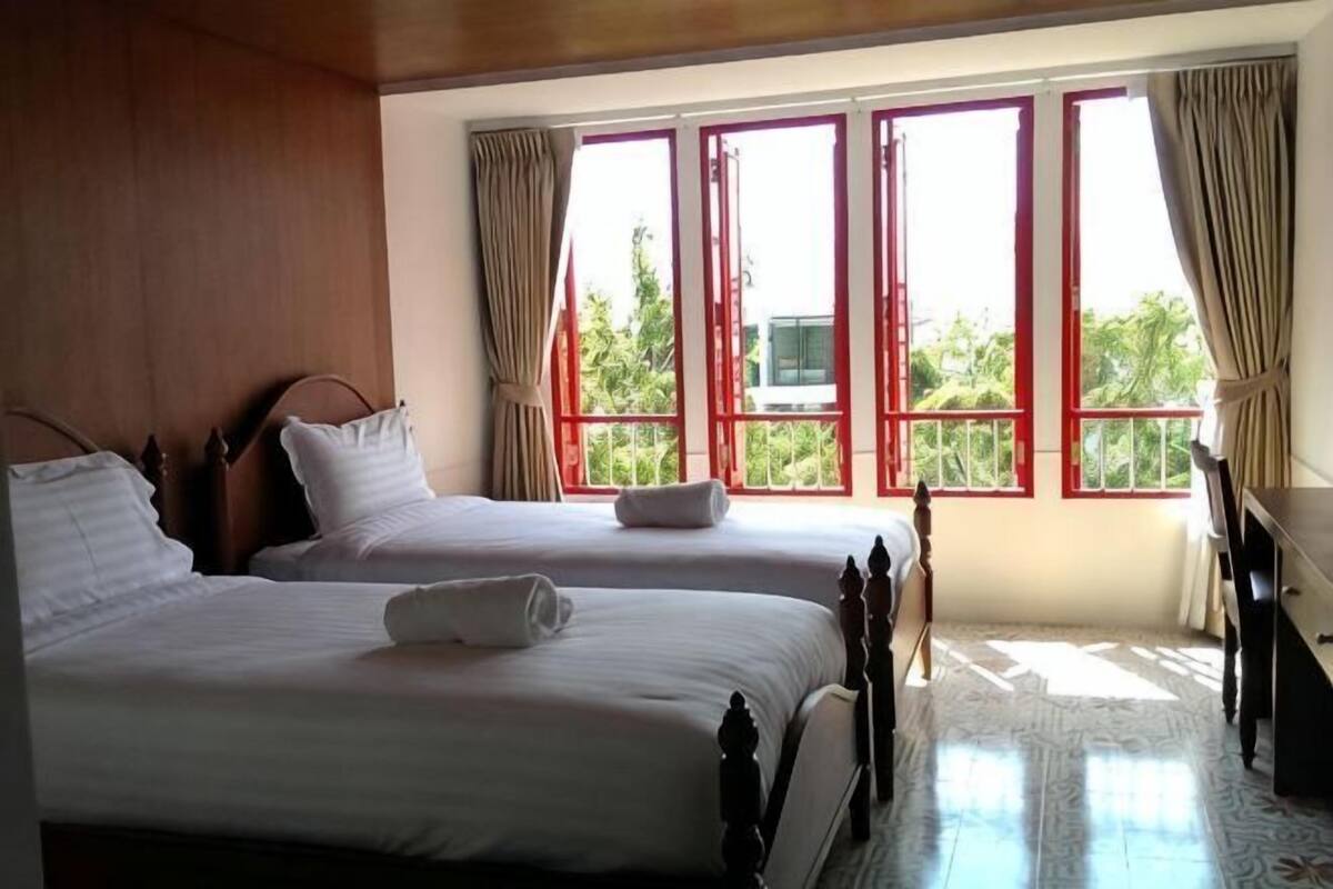 Une chambre avec deux lits, un plafond en bois et de grandes fenêtres avec des rideaux.