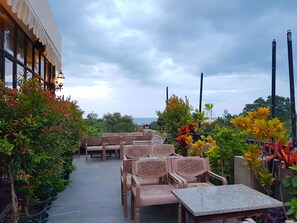 Un espace extérieur aménagé avec plusieurs tables et chaises, entouré de plantes en pot et d’arbres.