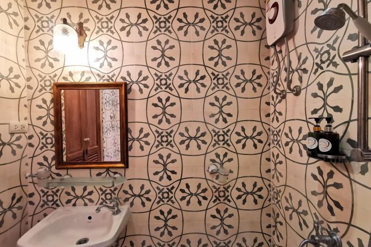 A bathroom with a patterned tile wall, a sink, a mirror, and a shower area.