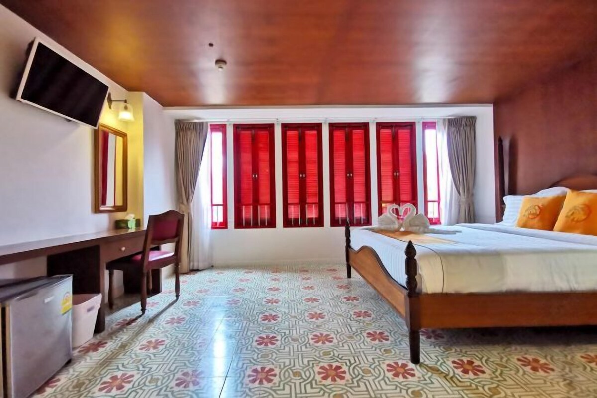 Een hotelkamer met een bed, een bureau, een stoel, een aan de muur bevestigde televisie en een raam met rode gordijnen.
