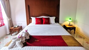 A neatly made bed with a red and white bedspread, two red pillows with a logo, a wooden headboard, a bedside table with a lamp, and a telephone. - Lertnimit Boutique Hotel (Hua Hin)