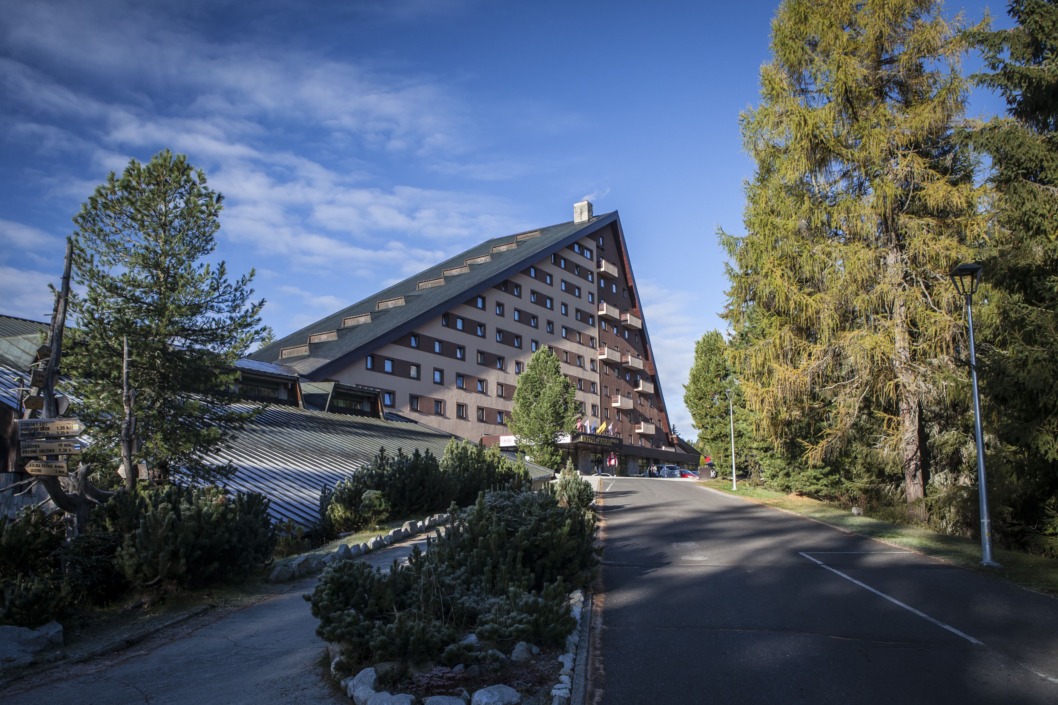 Un hotel moderno con un techo triangular distintivo, rodeado de árboles y un cielo despejado.