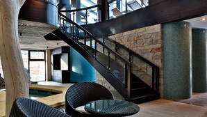 A modern interior with wicker furniture, a glass table, a stone wall, and a metal staircase. - Hotel Patria (Štrba)