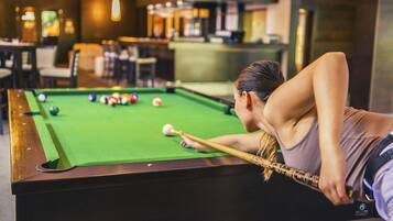 A pool table in a room with a bar and seating area in the background.