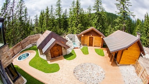 A wooden cabin complex with a hot tub, a stone patio, and a wooden deck. - Hotel Patria (Štrba)