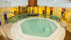Una amplia piscina interior con un desagüe central, rodeada por una solana con baldosas y barandales de metal.