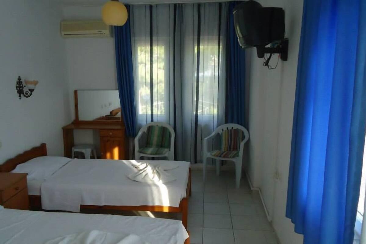 Une chambre d’hôtel avec deux lits, un bureau, une chaise, un téléviseur fixé au mur et des rideaux.