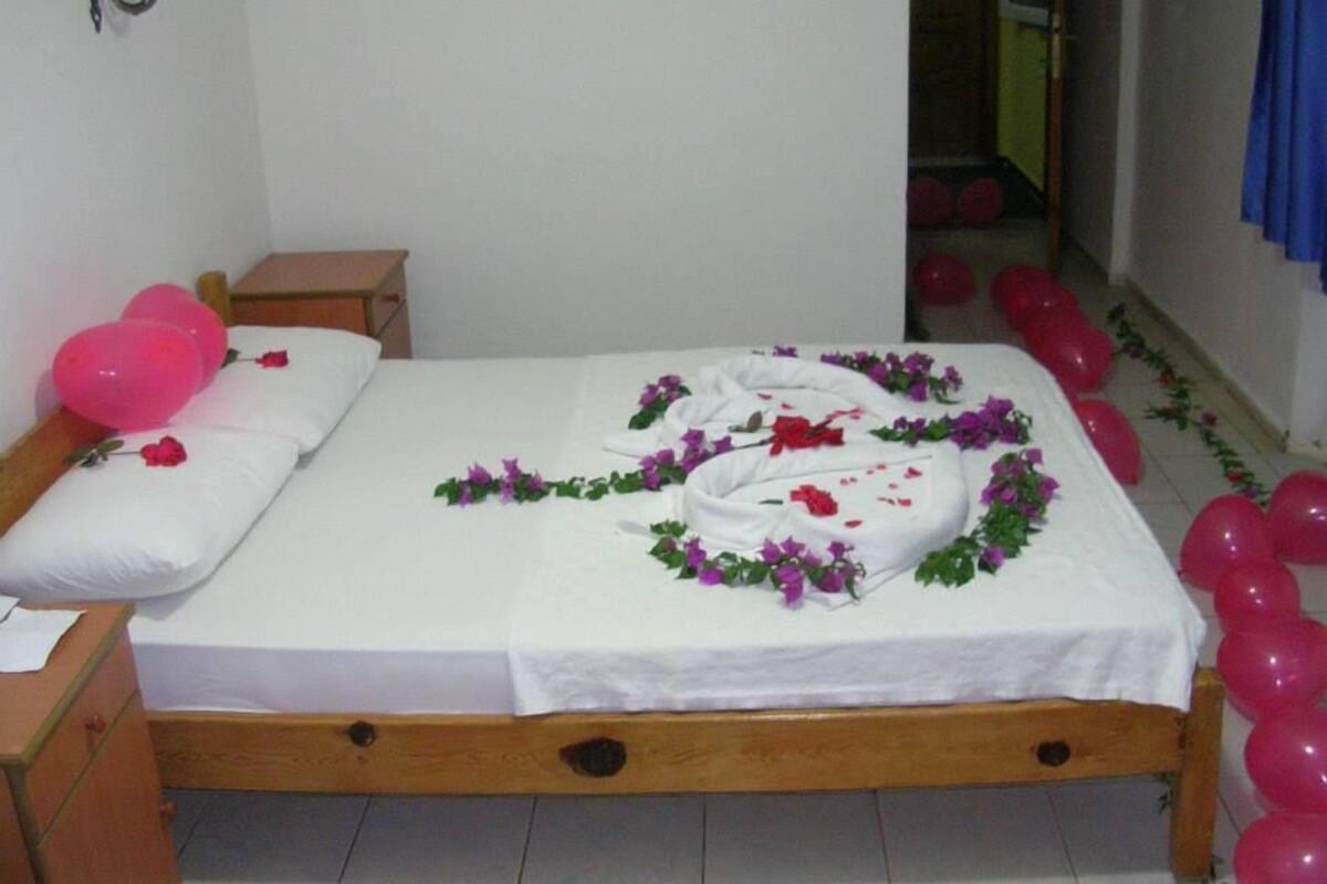 Un lit avec un drap blanc, des ballons roses et un arrangement floral.