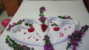A bed with a heart-shaped towel arrangement, pillows with rose decorations, and a bedside table with a phone and papers. - Hotel Babadag (Fethiye)