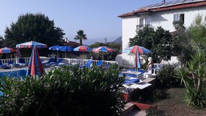 A pool area with sun umbrellas, lounge chairs, and a view of the mountains. - Hotel Babadag (Fethiye)