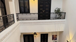 Une cour comprenant un canapé, une table et un espace vert. On y trouve deux portes et un balcon doté d’une balustrade.