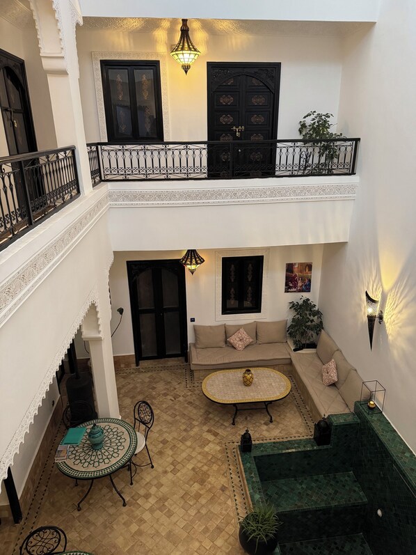 Un patio con un sofá, una mesa y una zona verde. Hay dos puertas y un balcón con barandilla.