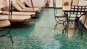Un espace extérieur ensoleillé, aménagé avec des fauteuils confortables et une table, le tout entouré de plantes en pot.