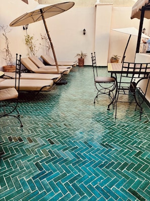 A sunlit outdoor seating area with lounge chairs and a table, surrounded by potted plants. - Dar Nossa (Marrakech)