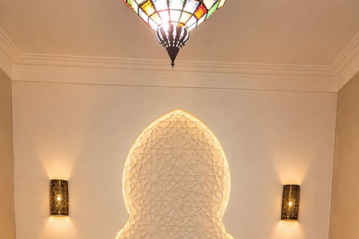 A bedroom with a large bed, decorative wall panels, two wall-mounted lamps, and a patterned floor.