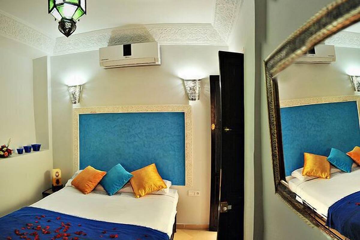 A hotel room with a large bed, a blue headboard, and a mirror on the wall.