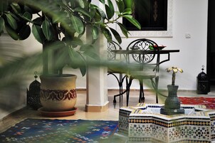 Quarto com planta em vaso, tapete estampado, cadeira de metal e mesa decorativa.