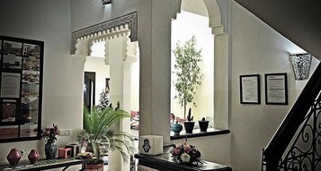 Um hall com escada, balcão de recepção, plantas em vasos e documentos emoldurados na parede.