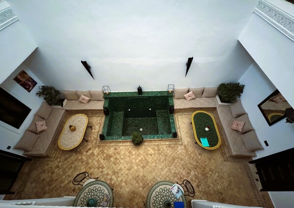 An indoor courtyard with a central swimming pool, seating areas, and decorative elements. - Dar Nossa (Marrakech)