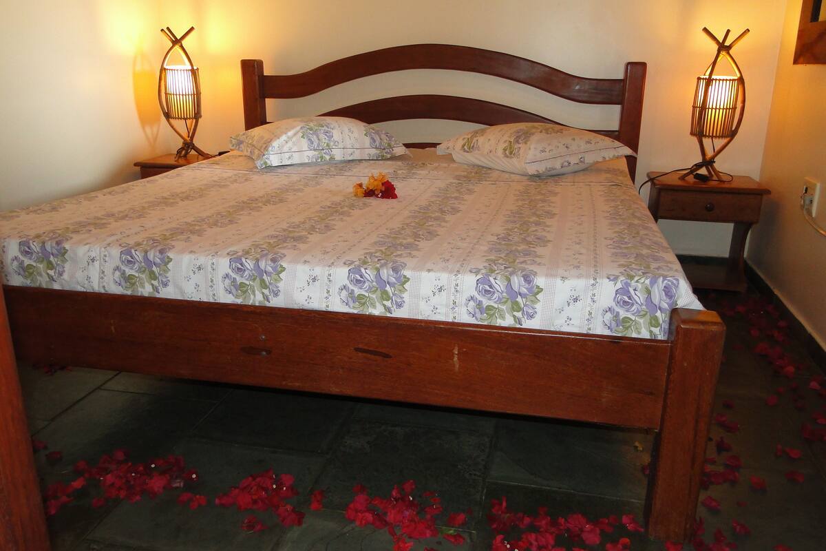 Un lit recouvert d’une couvre-lit à motifs floraux, deux lampes de chevet et des pétales de rose éparpillés sur le sol.