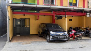 A black car parked in a covered parking area with a yellow building in the background. - Reddoorz near Gajah Mada Plaza 2 (Jakarta)
